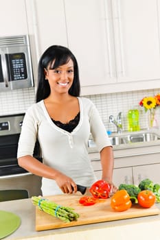 Smiling black woman cutting vegetables in modern kitchen interior