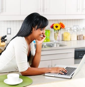 Smiling black woman using computer in modern kitchen interior