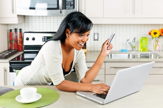Smiling black woman online shopping using computer and credit card in kitchen