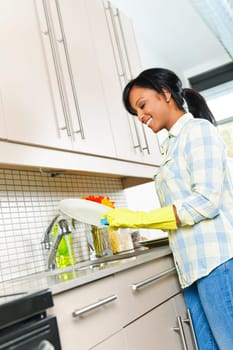 Smiling young black woman washing dishes in kitchen