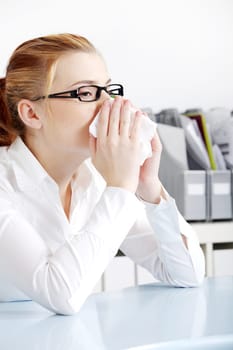 Caucasian woman in glasses sneezing in the office.