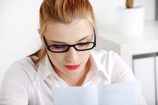 Closeup on young pretty woman in glasses reading files.