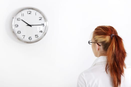 Caucasian businesswoman looking at white clock on the wall.