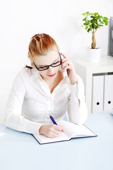 Pretty caucasian businesswoman answering the phone and writing.
