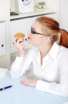 Beautiful caucasian woman in glasses smelling a cupcake in the office.