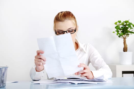 Sitting caucasian woman in glasses reading files behind the desk.