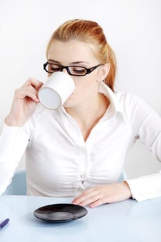 Sitting woman in glasses drinking coffee in the office.