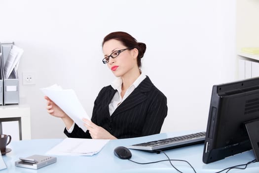Pretty caucasian businesswoman reading files behind the desk in the office.