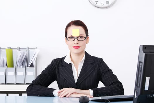 Pretty caucasian businesswoman sitting in the office with post it note on her forehead.