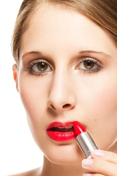 Close-up of a young woman applying lipstick on a white background