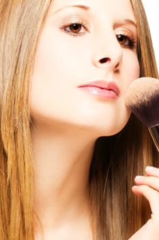 Young woman with brush applying makeup on white background