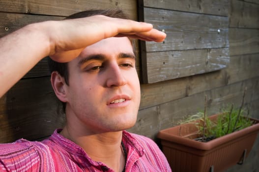 Head and shoulders portrait of a young man sitting in front of a wooden hut and looking at the sunset