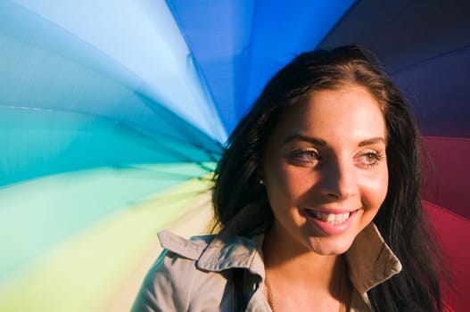 Head and shoulders portrait of a young black-haired woman with colorful umbrella as background