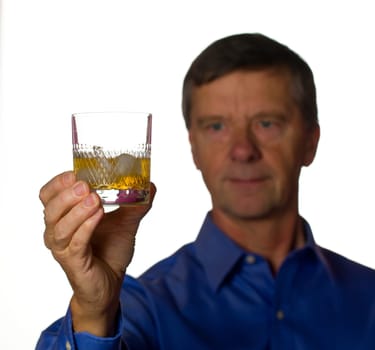 Senior retired male with a glass of scotch whiskey on ice in a cut glass with the man out of focus
