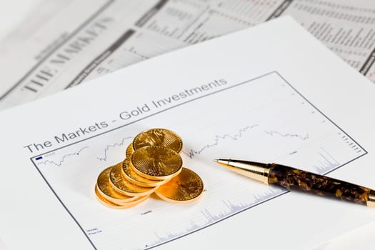 Gold Eagle one ounce coins stacked into graph of gold on business pages of newspaper with graphs showing drop in prices