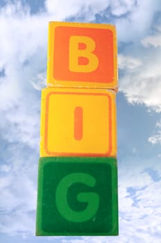 childrens toy letter building blocks against a cloudy background spelling big