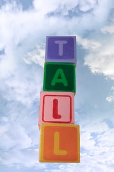 childrens toy letter building blocks against a cloudy background spelling tall with clipping path