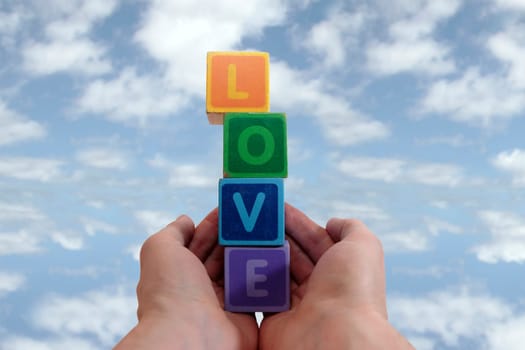 childrens toy letters in outstretched hands against cloudy background
