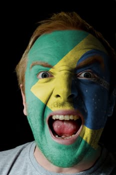 Low key portrait of an angry man whose face is painted in colors of brazilian flag