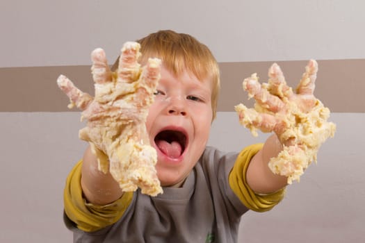 Boy makes dough for baking and proudly shows his sticky hands