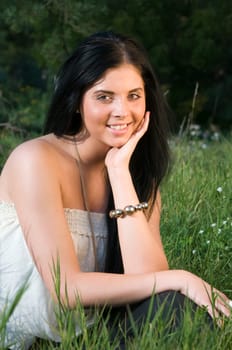 Upper body portrait of a young black-haired woman sitting on a meadow,resting her head on one hand and looking at the camera