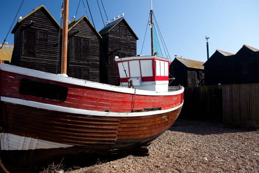 Fishing boat moored on coast next to fishing huts in village of Hastings in England. Red Ship and black architecture