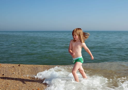 Child playing by water on beach in England. Boy in evening light on coast with waves