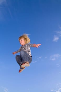 Child jumping in the sky. kid flying through the air. boy with long blond hair and sandals agains blue sky