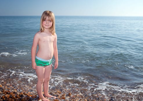 Child playing by water on beach in England. Boy in evening light on coast with waves