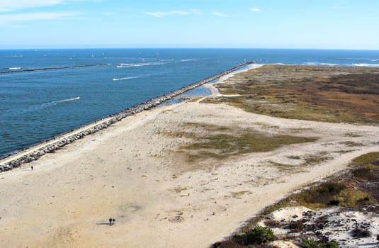 An aerial view of a coastline. Several boats can be seen coming in and out of an inlet.