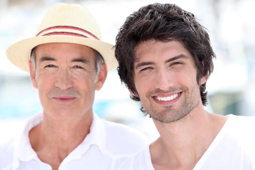 65 years old man wearing a straw hat and a 25 years old man posing in a summer vacation atmosphere