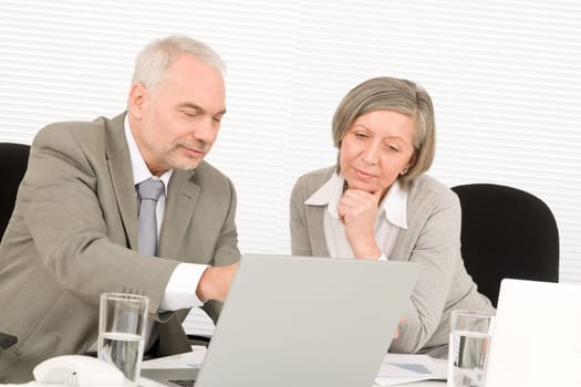 Professional senior businessman pointing at computer with woman colleague discussing
