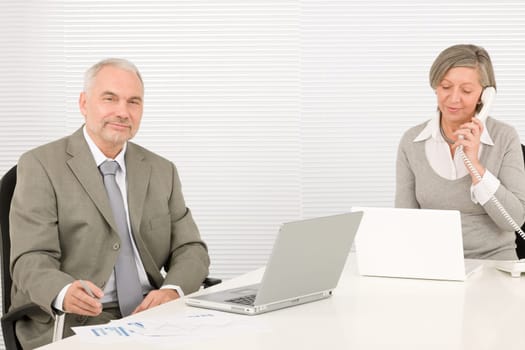 Professional elegant happy senior businesswoman looking graphs with man colleague