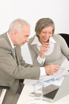 Professional elegant happy senior businesswoman looking graphs with man colleague