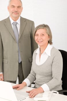 Professional senior businesswoman behind computer with male colleague