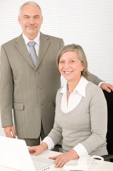 Professional senior businesswoman behind computer with male colleague