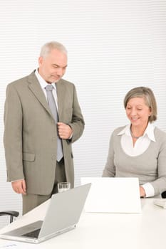 Professional senior businessman looking at computer with woman colleague