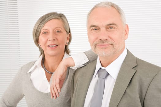 Professional elegant smiling senior businesswoman leaning against her male colleague