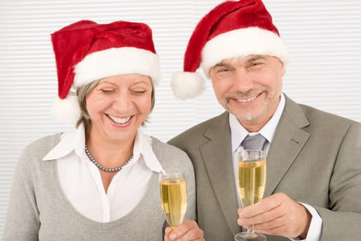 Laughing senior businesspeople in Christmas Santa hat drink champagne