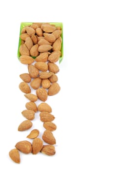 sliding down almond nuts from a green cup isolated on white background