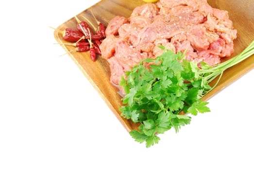 raw pork meat with red pepper and parsley ready to be cooked on a wooden tray (over white)