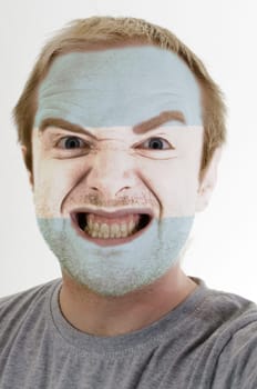 High key portrait of an angry man whose face is painted in colors of argentina flag