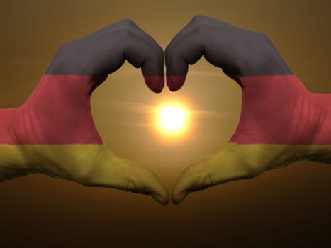 Gesture made by germany flag colored hands showing symbol of heart and love during sunrise