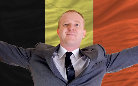 joyful investor spreading arms after good business investment in belgium, in front of flag