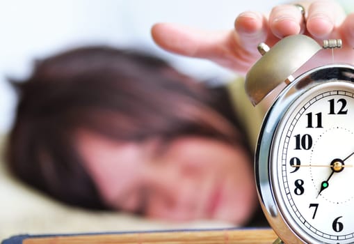A woman is sleeping with an alarm clock in front