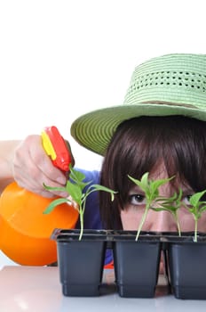 Young woman spraying water onto plants isolated on white background