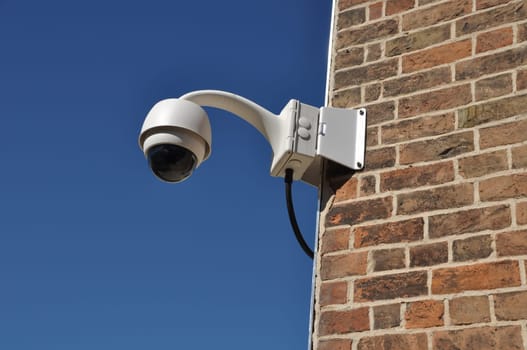 surveillance camera attached on a brick wall building (blue sky available)