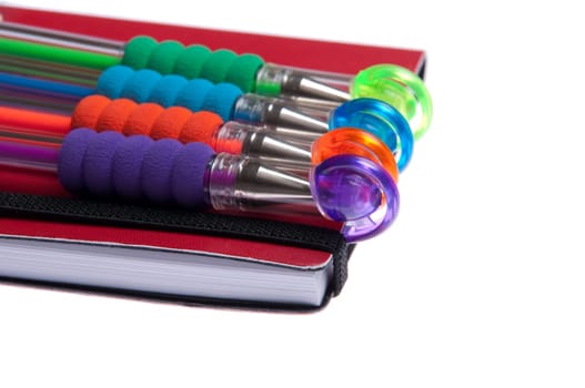 red notebook diary or agenda and colored pens lying on the top (isolated on white background)