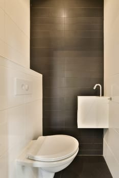 a white toilet in a black and white bathroom with dark tiles on the wall behind it is a small sink