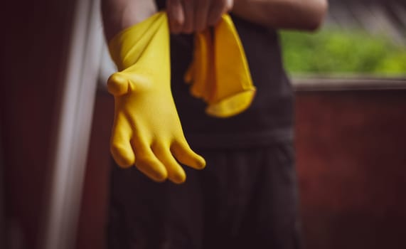 One young Caucasian unrecognizable male builder in black uniform puts on yellow rubber gloves, close-up view from below. The concept of home renovation, construction work.